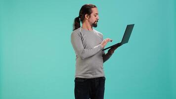 Portrait of smiling person spending time on laptop, isolated over studio background. Cheerful man checking social media posts on notebook, enjoying leisure time, camera A video