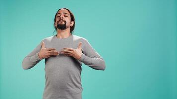 Portrait of man inhaling and exhaling to relax and gain positive energy, eliminating stress. Person doing breathing exercises for wellbeing, isolated over studio background, camera B video