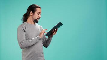 man bläddring fastän finansiell granska Rapportera på läsplatta, isolerat över blå studio bakgrund. arbetstagare läsning pappersarbete på digital bärbar enhet, lösning företag uppgifter, kamera b video