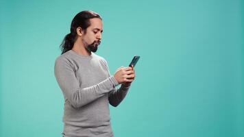 Smiling man having friendly conversation with friends during teleconference meeting using smartphone, studio background. Person having fun catching up with mates during online videocall, camera B video