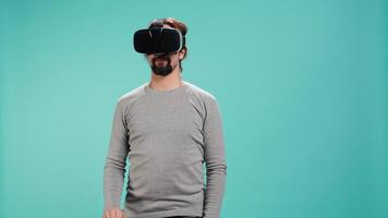 Tech enthusiast wearing virtual reality goggles, doing zooming in gestures. Arab man using high tech futuristic modern VR glasses, making tactile touching gesturing, studio background, camera B video