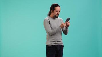 Man holding mobile phone, browsing betting website, celebrating after winning money, isolated over studio background. Cheerful person feeling happy while scrolling on smartphone, camera A video
