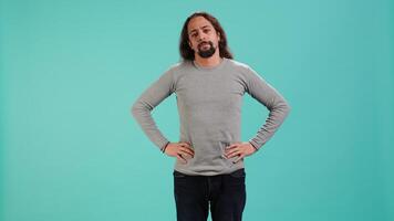 Portrait of man standing confidently with hands on hips, posing against plain studio background, projecting confidence and strength. Person holding assertive stance posture, camera A video