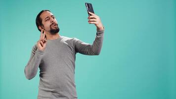 Man using smartphone to take selfies and post them on social media, studio backdrop. Vain person taking photos using phone selfie camera, isolated over studio background, camera B video