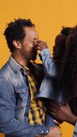 vertical retrato de africano americano familia con un pequeño chico posando en estudio, demostración afecto y amor hacia cada otro y sensación contento. agradecido marido y esposa participación su niño pequeño. cámara b. video