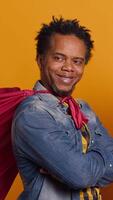 Vertical African american dad being the superhero of his little toddler, posing as a hero with a red cape and saving his family from any danger. Cute loving family posing against yellow background. Camera A. video