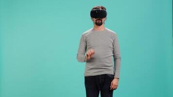 Man wearing virtual reality headset, interacting with interface, doing swiping motions. Person having fun using high tech futuristic modern VR gadget, isolated over blue studio background, camera A video