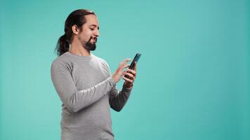 Man scrolling on smartphone touchscreen, using mobile phone to check social media feed, studio backdrop. Person browsing internet websites, isolated over studio background, camera B video