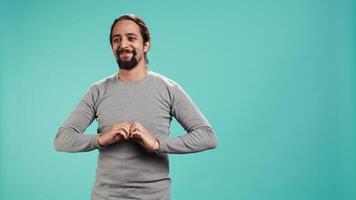 Portrait of joyful friendly man doing heart symbol shape gesture with hands. Smiling nurturing person showing love gesturing, isolated over blue studio background, camera B video