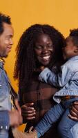 Vertical African american positive couple doing peek a boo with their young child in studio, smiling people hugging together. Happy affectionate mom and dad showing gratitude and respect. Camera B. video