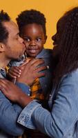 vertical retrato de africano americano familia con un pequeño niño posando en cámara, demostración gratitud y simpatía hacia cada otro y sensación satisfecho. contento mamá y papá participación su chico. cámara una. video