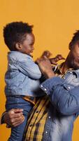Vertical Playful smiling father embracing his cute infant toddler in studio, african american caring dad playing around with his little boy. Loving parent laughing and feeling happy with his son. Camera B. video