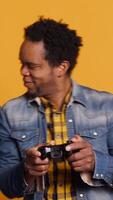 Vertical African american life partners playing games together in studio, having fun and enjoying leisure time with their controllers. Cheerful smiling married couple in a competition. Camera A. video