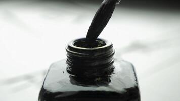 Female hand dunks brush in a jar of ink for drawing close up. Chinese Old-fashioned Paint Brushes with Selective Focus. Detail of a chinese brush while drawing a line in light back photo