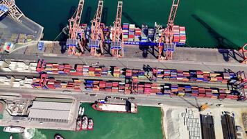 Cranes loading and unloading cargo create a lively scene at a bustling port, highlighting dockworkers as they maneuver containers under bright, sunny skies video