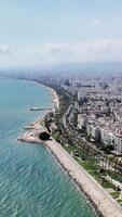 Camera panning over a coastal city with white buildings, a beach, and mountains in the background. The blue sea is calm and serene video