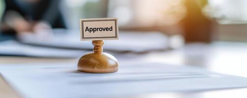 A wooden stamp with the word 'Approved' placed on documents, symbolizing success, acceptance, and validation in a professional setting with a soft focus background. photo