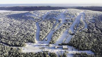 Aerial of the ski resort with funicular in the snowy forest in a sunny day. Footage. Winter landscape of snowy mountain slope among pine trees on blue sky background. photo