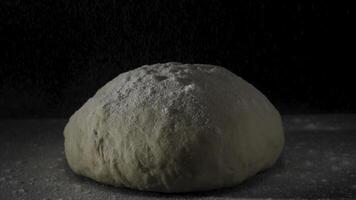 Four falling on fresh raw dough on black background in slow motion. Frame. Cook sifts the flour for the dough. Sprinkling flour over fresh dough on kitchen table. Fresh raw dough for pizza or bread photo