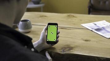 View over the shoulder of a businessman using the hand held cellphone with green screen touchpad on wooden table background. Stock footage. Man lloking at his device, chromakey. photo