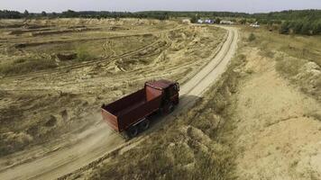 Aerial for the red big truck driving in ground quarry with flying dust behind it, industry concept. Scene. Empty lorry moving on country road with green forest on the background. photo