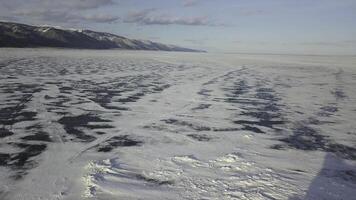 Stunning natural landscape of Siberian wild nature. Clip. Aerial view of ice and snow surface of Lake Baikal in the background Olkhon island in a winter cloudy day. photo