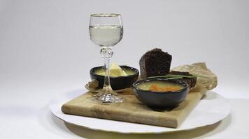 Fresh red caviar with basil and butter on bread in studio. Bred with red caviar with wine glasses on background. Cold Russian vodka with ice and small snacks with butter and red caviar photo