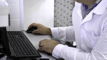 Close-up of man in white coat sitting at computer. Man in white coat sitting at computer in white room is doctor or scientist photo