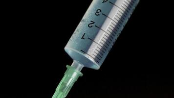Taking vaccine into a glass syringe from a ampule on a black background. Closeup. Syringe is typed in turquoise fluid injection from illness serious illnesses, the concept of medicine photo
