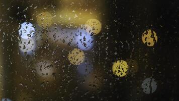Close-up of the blurred light spots through the window and raindrops falling down on the glass at the evening. Concept. Rainy weather photo