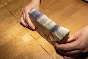 A person holding a stack of money on a table photo