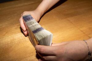 A person holding a stack of money on a table photo