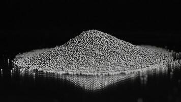 Rotating pile of rocks isolated on black background. Stock footage. Close up of tiny black pieces of gravel spinning while lying on the reflective surface. photo