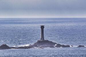 Solitary Lighthouse on Rocky Outcrop at Land's End in Cornwall, UK photo