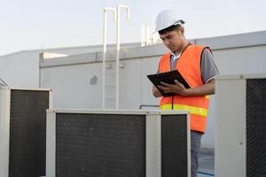 Asian maintenance engineer works on the roof of factory. contractor inspect compressor system and plans installation of air condition systems in construction. Checklist, inspector, control photo