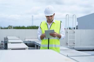 Asian maintenance engineer works on the roof of factory. contractor inspect compressor system and plans installation of air condition systems in construction. technology, online, mobile application. photo