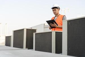 Asian maintenance engineer works on the roof of factory. contractor inspect compressor system and plans installation of air condition systems in construction. Checklist, inspector, control photo