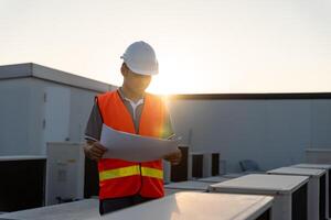 Asian maintenance engineer works on the roof of factory. contractor inspect compressor system and plans installation of air condition systems in construction. Blueprint, inspector, control photo