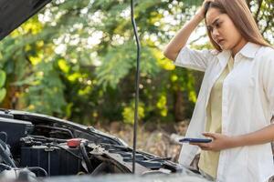 breakdown, broken car, repair. Woman uses mobile phone check insurance premiums through application due to car accident . Find garage to get car fixed during country tour, waiting for help, emergency. photo