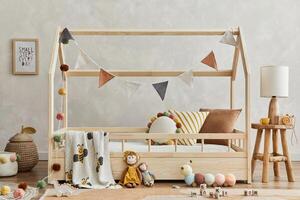 Stylish composition of cozy scandi child's room interior with wooden bed, pillows, elegant lamp, plush and wooden toys and textile hanging decorations. Creative wall, carpet on the floor. Template. photo