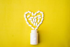The heart made of tablets and pills on yellow background. Assorted pharmaceutical medicine pills, tablets and capsules and bottle on yellow background. Flat lay. Copy space. Medicine concept photo