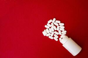 Pills spilling out of pill bottle and isolated on red. with copy space. Medicine concept photo