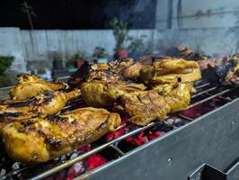 Grilled chicken sizzling on a charcoal barbecue during a night gathering in a backyard with warm light illuminating the delicious smoky feast photo