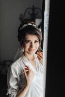 A woman in a white dress is smiling and looking out a window. The image has a warm and inviting mood, with the woman's smile and the light coming in through the window photo