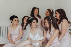 A group of women are sitting together, one of them is wearing a wedding dress. They are all smiling and seem to be enjoying each other's company photo