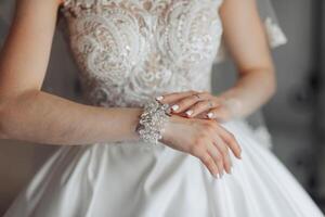 A woman is wearing a white dress and a bracelet. She is looking at the camera. The bracelet is made of crystals and is on her wrist photo