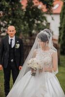A bride and groom are standing in a field with a white veil over the bride's face. The bride is holding a bouquet of flowers photo