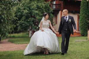 A bride and groom are walking down a grassy path. The bride is wearing a white dress and the groom is wearing a suit. They are holding hands and seem to be enjoying their time together photo