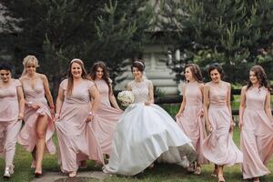 A group of women are walking down a path, one of them is wearing a white dress. The bride is walking with her bridesmaids, and they are all dressed in pink photo
