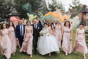 A bride and groom are surrounded by their wedding party, all dressed in pink. The bride is wearing a white dress and the groom is wearing a blue suit photo